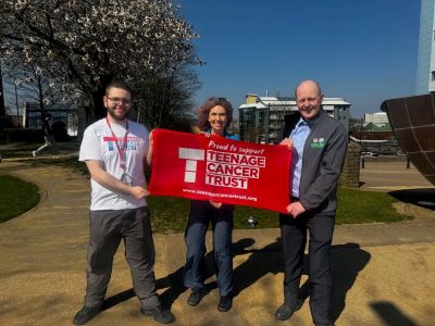 Chris Hart and a lady and student holding a red flag with Teenage Cancer Trust logo on it